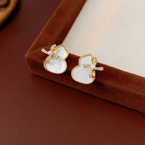 Macro shot of gold gourd earrings with white mother-of-pearl and crystal bows on velvet