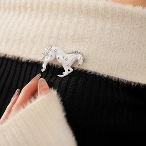 Detailed close-up of a vintage horse brooch with white enamel and sparkling rhinestones