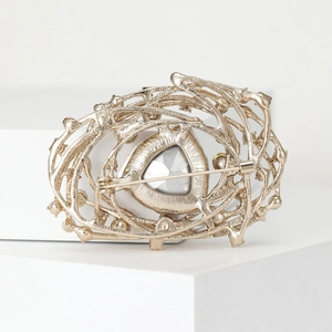 Vintage nest brooch in gold finish with large silver gemstone on a white pedestal