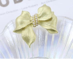 Detail of matte gold bow brooch with double-row pearls and brushed metal texture