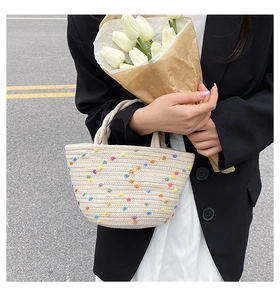 Detail of woven straw bucket bag with colorful pom poms and elegant double handles