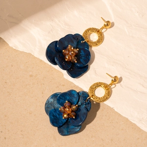 Détail de boucles d'oreilles fleurs bleues en résine avec anneau doré et perles ambre