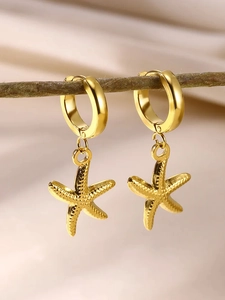 Macro shot of gold starfish earrings hanging on a branch with soft fabric background