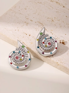 Detailed view of silver spiral earrings with colorful crystals on a beige stone