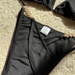 Detail of black bikini bottoms with pearl bead side straps and S-size fabric care label