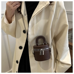 Petit sac seau cylindrique marron foncé avec bandoulière chaîne sur trench-coat beige