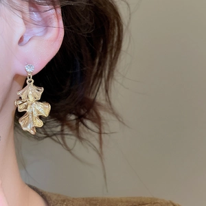 Close-up of golden ginkgo leaf earrings with crystal studs on female model