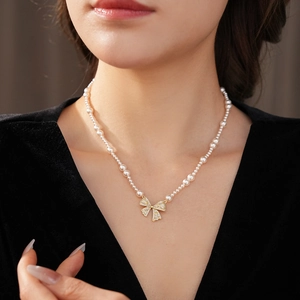 Detail of a pearl necklace with a golden bow pendant worn on a female neck