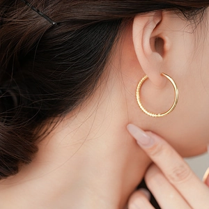 Minimalist geometric gold hoop earrings with textured finish worn by a fashion model
