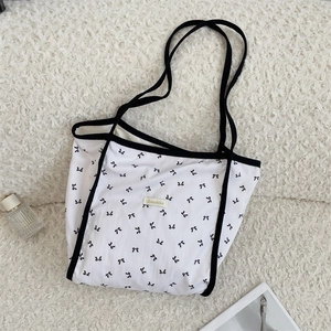 Vista piatta di una borsa shopper bianca con motivi a fiocco nero ed etichetta in tessuto