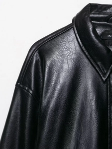 Detailed close-up of faux leather texture and shoulder stitching on a black aviator jacket