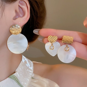 Dettaglio di orecchini a cuore in oro 24k con madreperla e motivo a griglia lucido