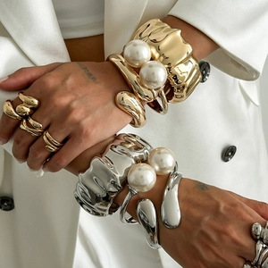 Close-up of golden and silver irregular metal bracelets with large white pearls on a model