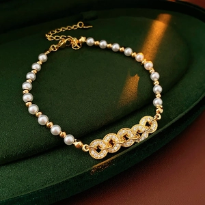 Detailed shot of gold and pearl beaded bracelet with zircon rings on green velvet tray