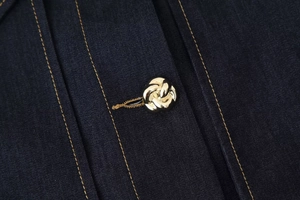 Gros plan du bouton en métal doré sur veste en jean bleu avec coutures contrastées