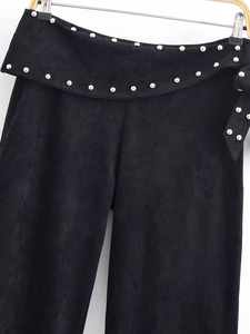 Detailed view of black suede flared trousers featuring silver metal stud embellishments