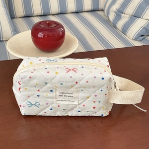 Detailed macro of cream quilted cosmetic bag with colorful dots and bow pattern