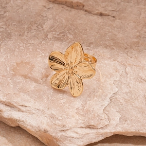 Macro shot of a golden flower ring with textured petals on a light stone background
