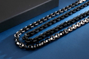 Detail view of thick stainless steel necklaces in black and silver on textured background