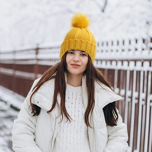 Outdoor shot of a mustard yellow knit beanie with a large pom-pom in snowy winter setting