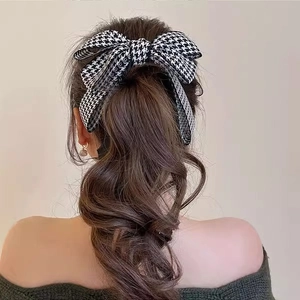 Detail of a chic black and white houndstooth bow hair clip on a ponytail