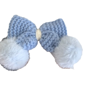 Blue knitted bow hair clip with white faux fur pom-poms on a clean white background