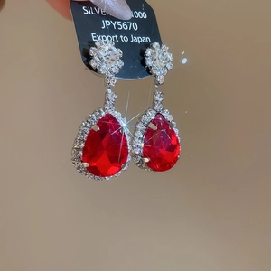 Dettaglio macro di orecchini a goccia rossi con marchio argento 1000 e cristalli scintillanti
