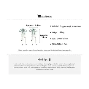 Detail view of long bow tassel earrings with green acrylic leaf charms and rhinestones
