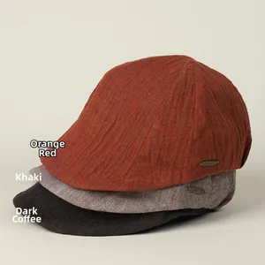 Close-up of stacked linen newsboy caps in orange, khaki, and brown with metal logos