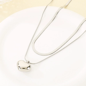 Detail view of double-layered silver necklace with snake chain and heart pendant