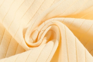 Macro detail of cream yellow ribbed cotton fabric showing soft texture and elastic weave