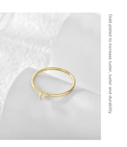 Close-up of a gold-plated four-prong ring with clear zircon on a white textured stone