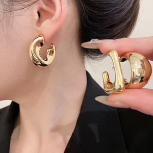 Close-up of chunky gold C-shaped hoop earrings with a polished mirror finish surface