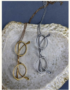 Detail of gold and silver eyeglass pendant necklaces with textured frames on a ceramic dish