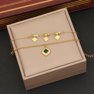 Detail of double-layer gold anklet with colorful beads and green gemstone pendant
