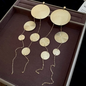 Macro detail of long gold metal tassel earrings featuring hammered circular discs on dark tray