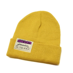 Close-up of yellow knit beanie with creative boarding pass style patch and ribbed texture