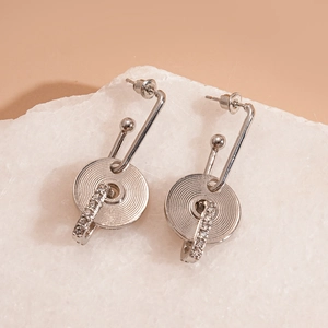 Silver geometric hollow earrings with textured disc and crystal circle on marble stand