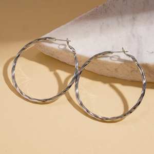 Macro shot of twisted silver hoop earrings showing S925 hallmark on white marble