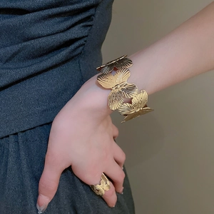Detail of golden metal leaf textured open cuff bracelet and matching ring on model