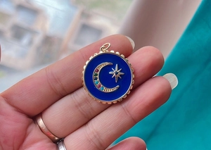 Detail of a celestial necklace pendant with a blue enamel moon and gold star charm