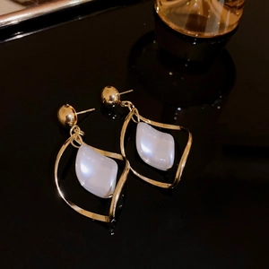 Detailed close-up of golden star earrings with white baroque pearls on black background
