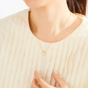 Close-up of a white pearl pendant on a gold O-chain necklace worn by a female model