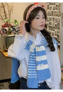 Detail of blue and white striped knit shawl with brand label worn over a shirt