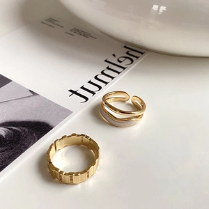 Detail of gold geometric textured and white enamel streamline rings on a white table