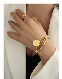 Détail du bracelet perlé doré à plusieurs rangs avec charms gravés et une bague