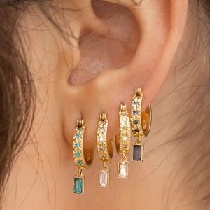 Detail of four gold hoop earrings with colorful rectangular zircon charms on ear