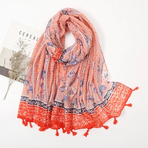 Flat lay of an orange cotton linen floral scarf with tassels and decorative cereal magazine