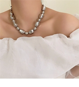 Close-up of irregular silver beads necklace worn by model in elegant white outfit