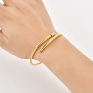 Detailed close-up of a golden twisted cable cuff bracelet worn on a woman's wrist
